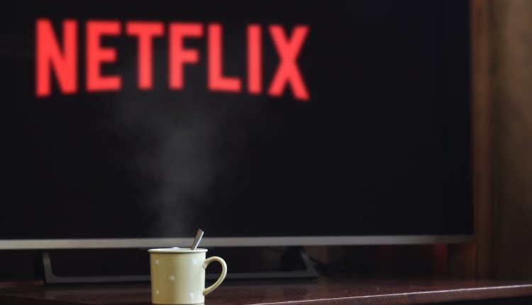 Foto de uma tela de televisão com o logo da Netflix e uma xícara de café sob a estante