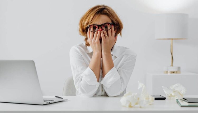 imagem de mulher sentada à mesa de um escritório com as mãos no rosto precisando aliviar o estresse